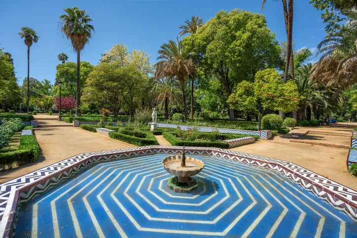 Fuente de azulejos azules y blancos rodeada de palmeras y setos en una glorieta del Parque de María Luisa