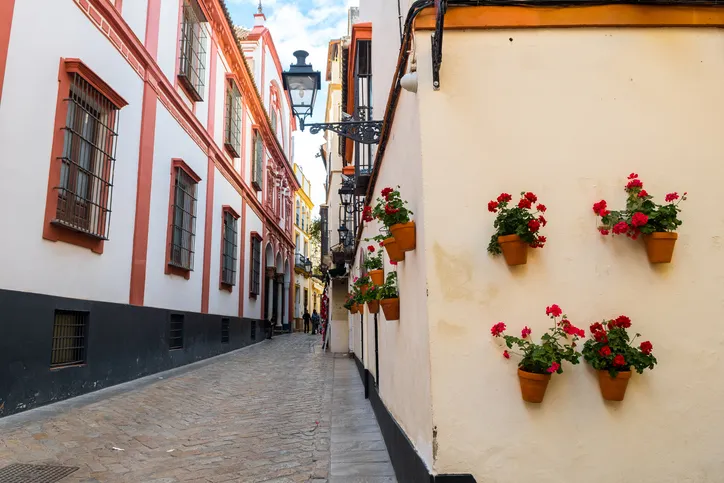 Calle del barrio de Triana con casas encaladas, rejas en las ventanas y macetas de geranios rojos en la pared