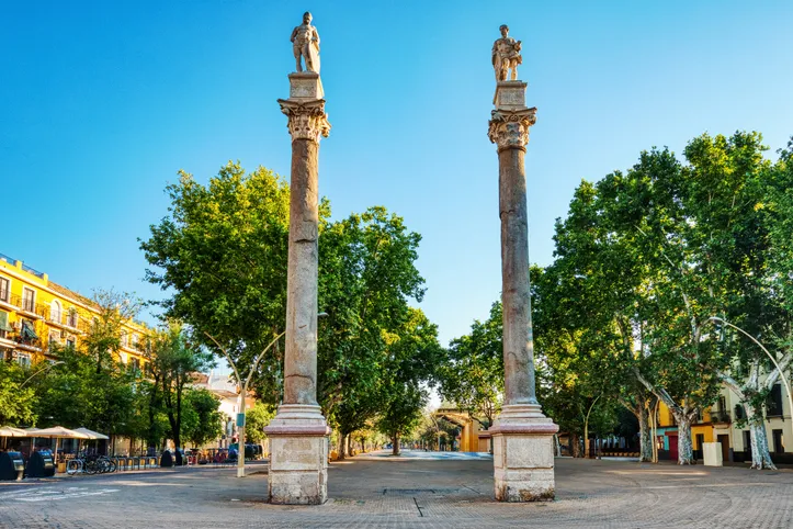 Columnas romanas de Hércules y Julio César en la Alameda de Hércules de Sevilla, entre árboles y edificios bajo un cielo azul