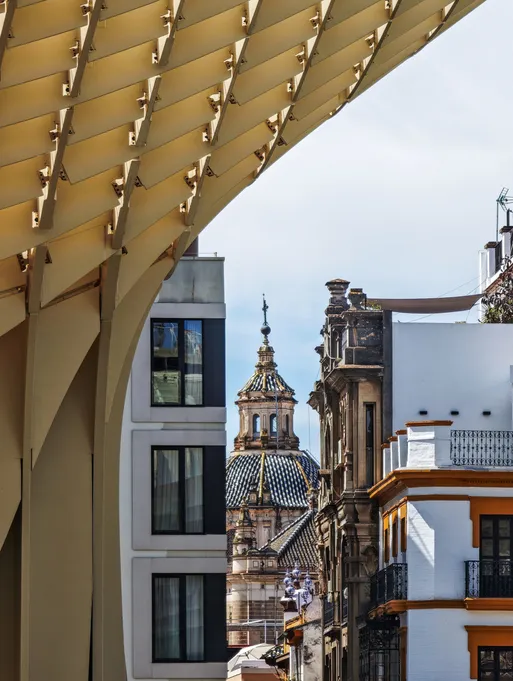 Detalle de la estructura de madera de Metropol Parasol junto a edificios históricos y la cúpula de una iglesia en Sevilla