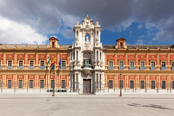 Fachada principal del Palacio de San Telmo en Sevilla, de ladrillo rojo con la portada barroca en el centro y las banderas en la entrada